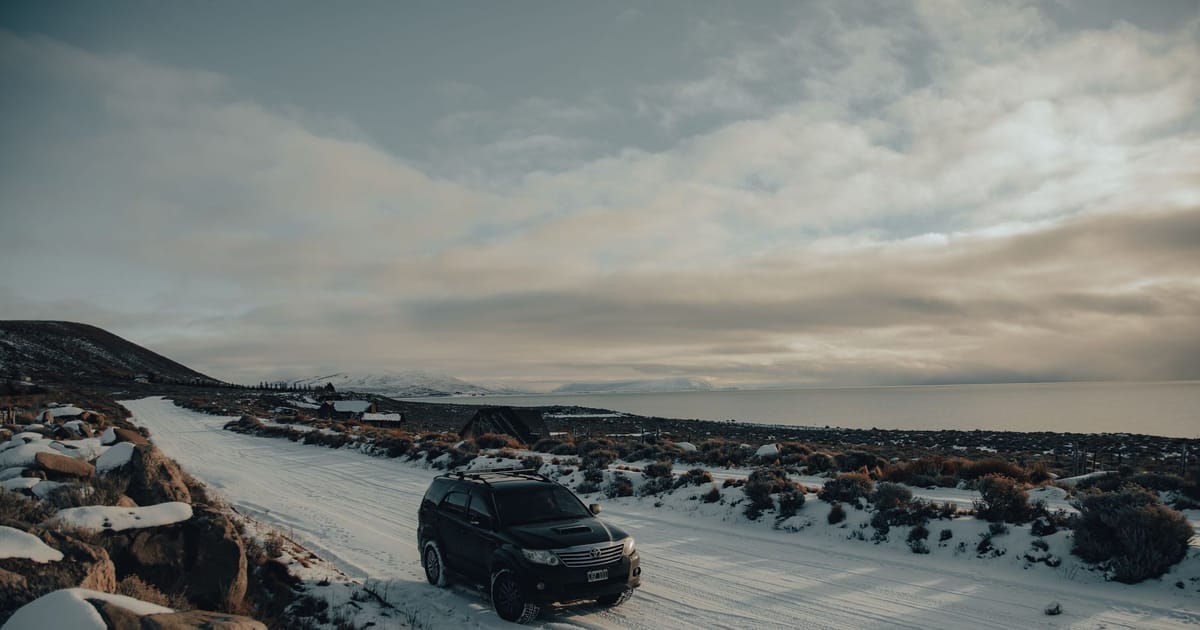 An SUV on a snow-covered track in open winter landscape.