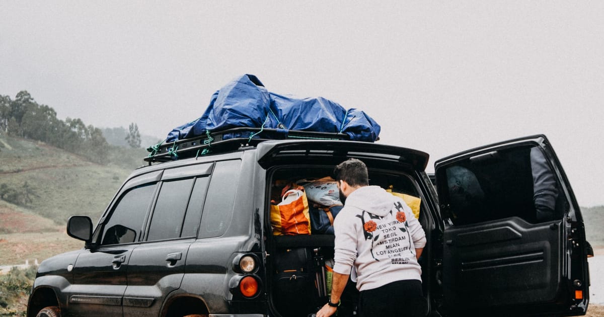 A person loading luggage into a packed estate car with a full roof rack.