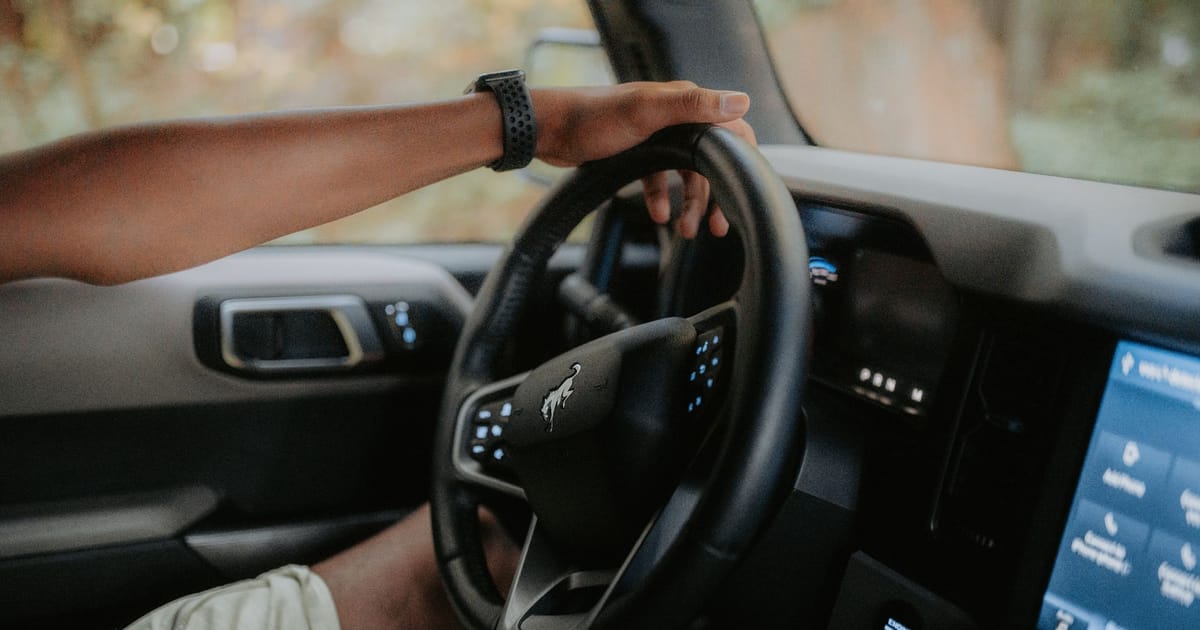 A hand resting on the steering wheel of a modern car.